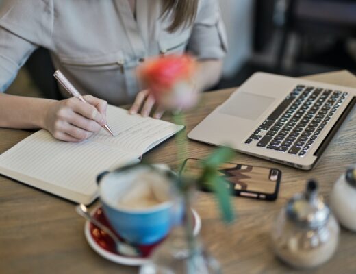 person writing on a notebook beside macbook