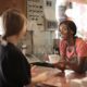 delighted black female barista serving coffee in cup in cafe