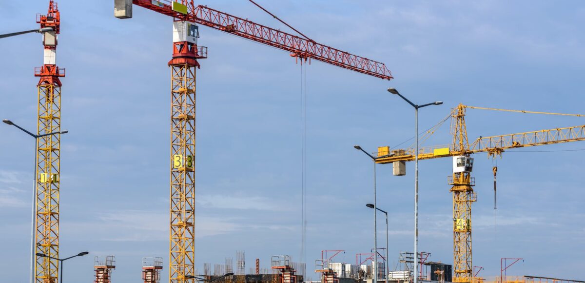 three yellow and red tower cranes under clear blue sky