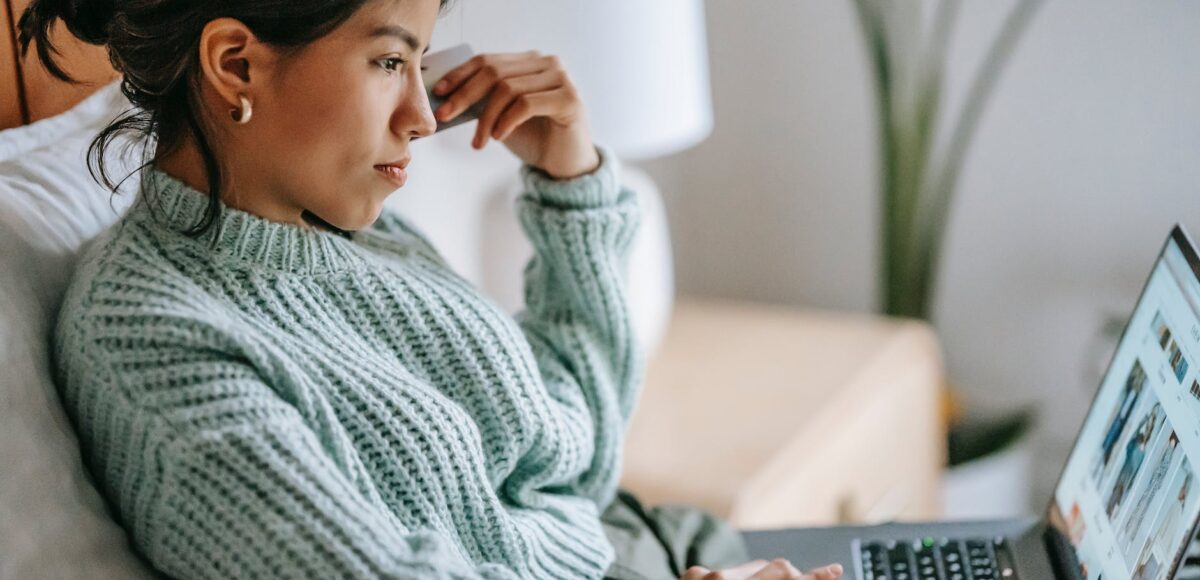 focused young ethnic woman with credit card and laptop