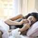 woman lying on bed while blowing her nose