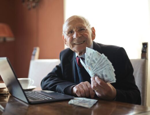 happy senior businessman holding money in hand while working on laptop at table