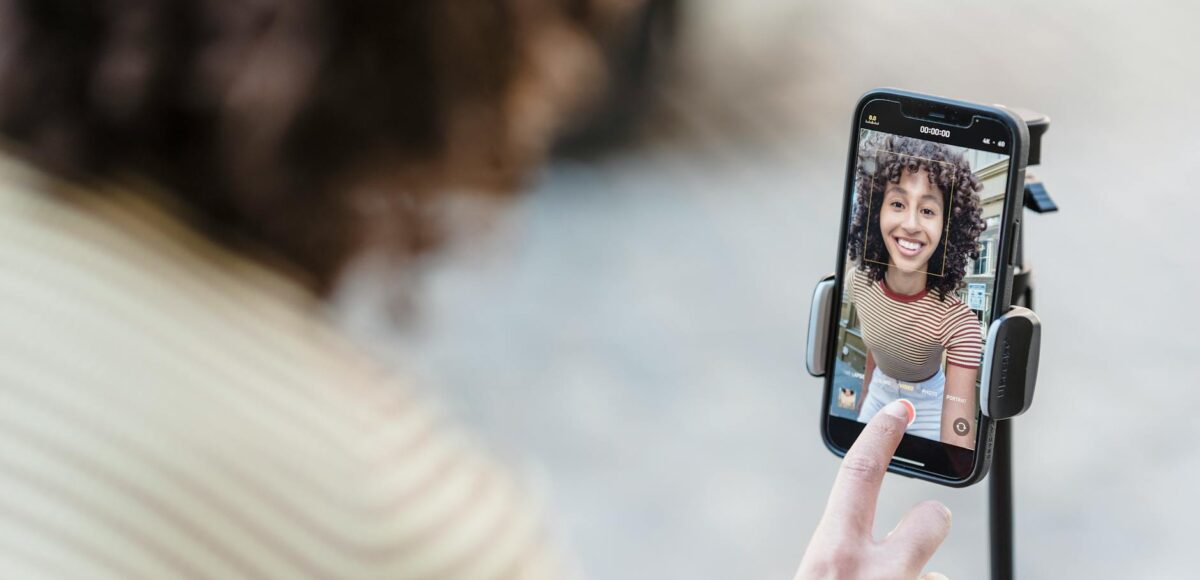 crop smiling ethnic blogger recording video on smartphone on street