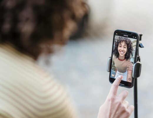 crop smiling ethnic blogger recording video on smartphone on street